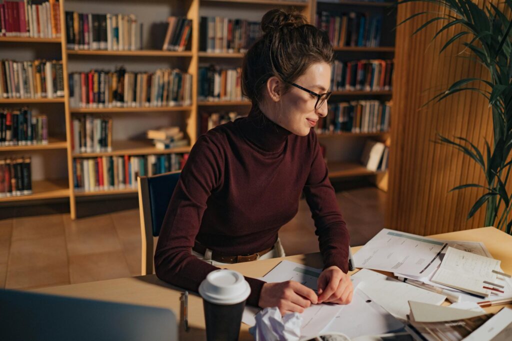 graduate student studying at university library surrounded by scholarship application papers