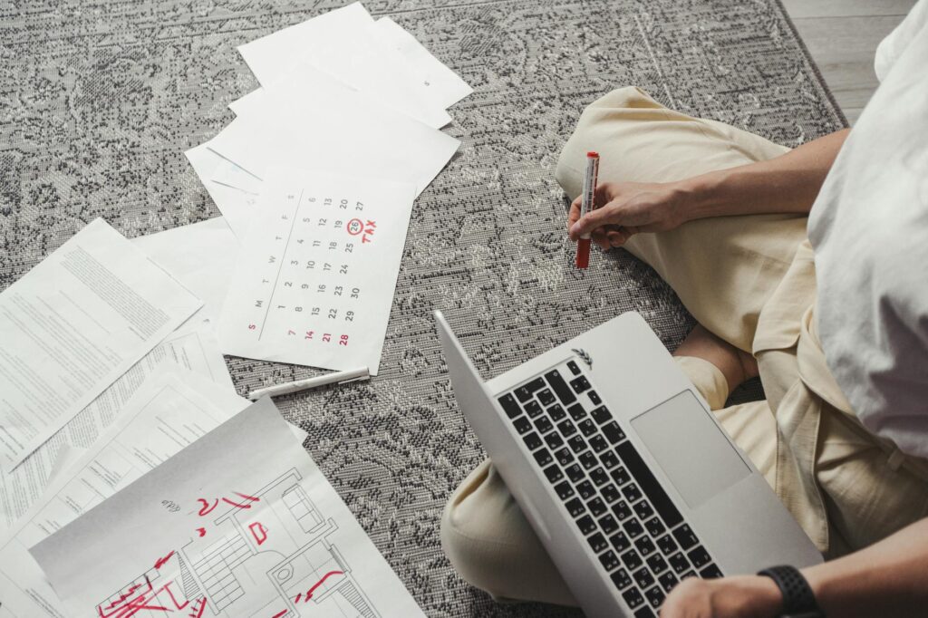 person organizing grant application documents on desk with laptop calendar open