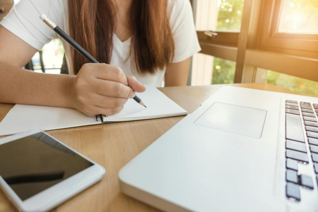 professional young woman writing scholarship application at desk with laptop and notebook
