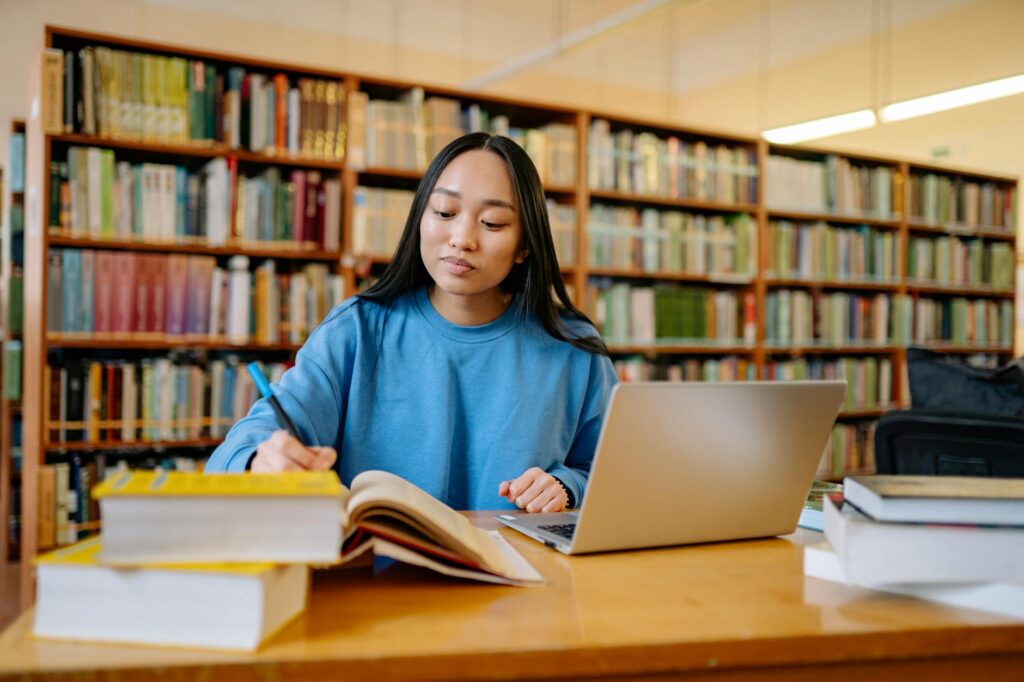 woman student smiling while reviewing scholarship application on laptop at university library